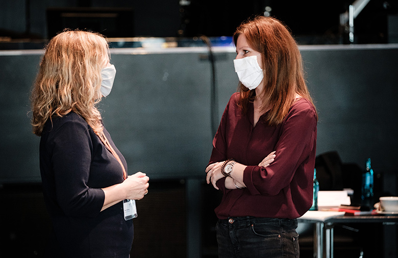 Zwei Frauen stehend  im Gespräch. Beide tragen Masken.